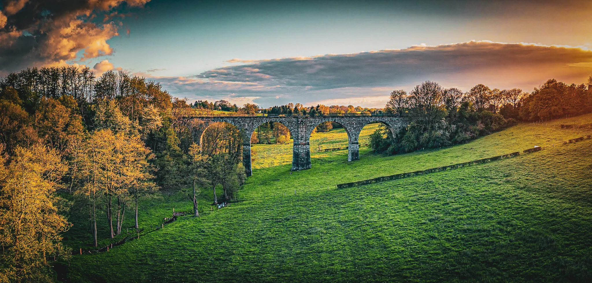 Een majestueus viaduct dat uitkijkt over weelderige groene weiden, onder een betoverende schemerhemel.