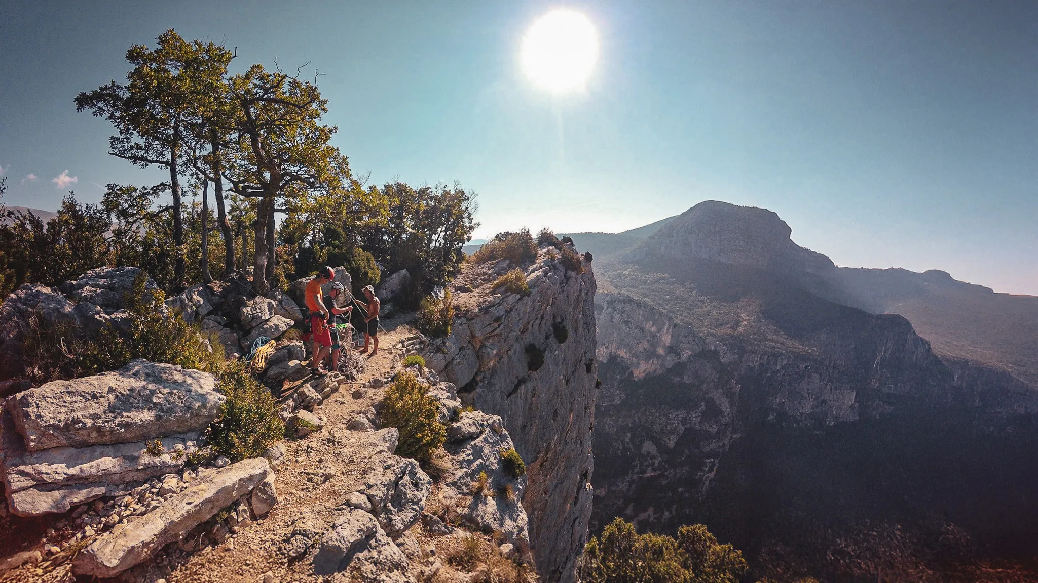A group of climbers prepare their equipment on a sunny cliff overlooking the Gorges du Verdon.
