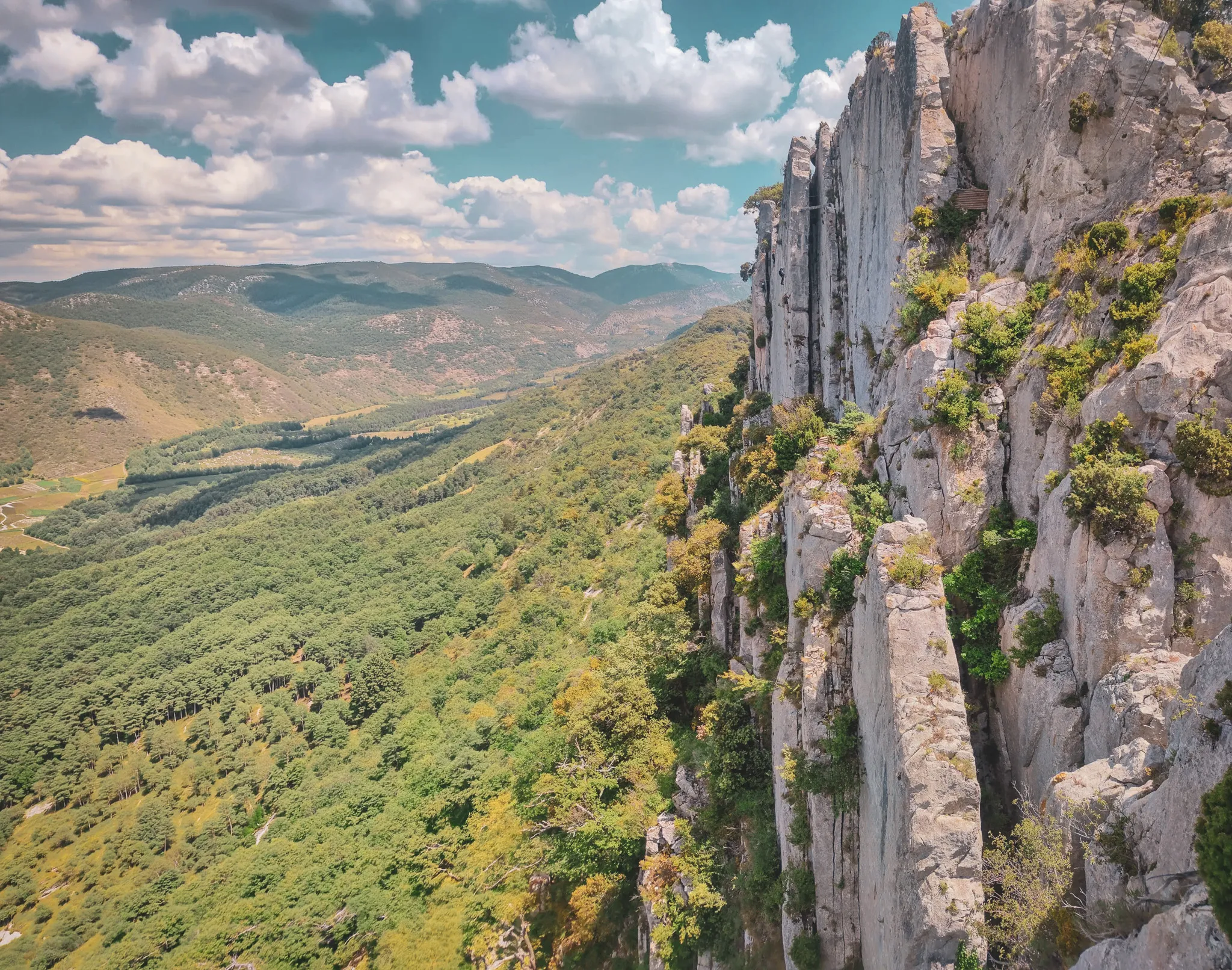 Panoramic views of the Dentelles de Montmirail, majestic cliffs and lush greenery under a blue sky.
