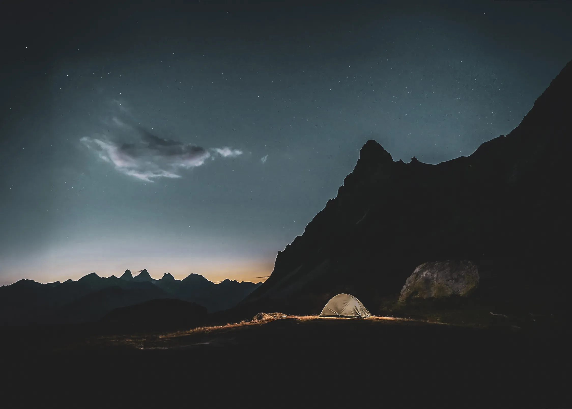 Tente de bivouac éclairée de l'intérieur sous un ciel étoilé, dans les Écrins