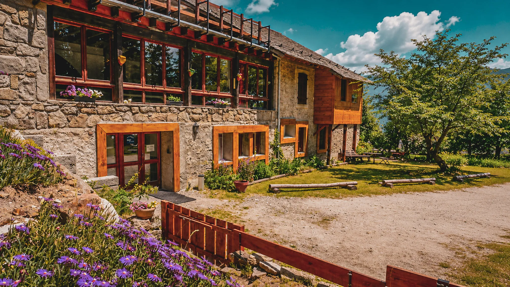 Gîte van natuursteen in het hart van de Pyreneeën, omringd door bloemen en met uitzicht op een weelderig landschap.