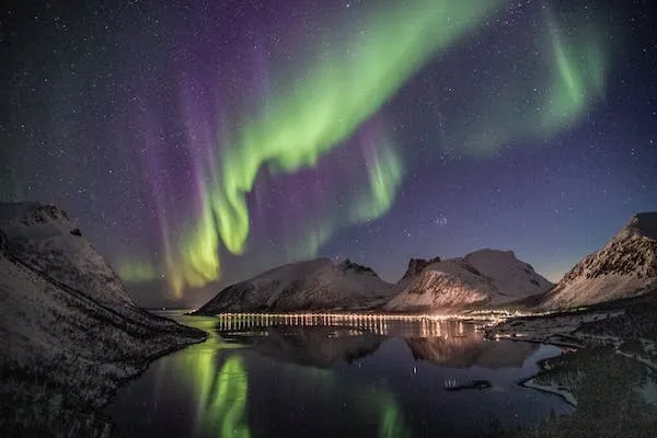 Aurore boréale entre montagne et village illuminé. Pic solaire 