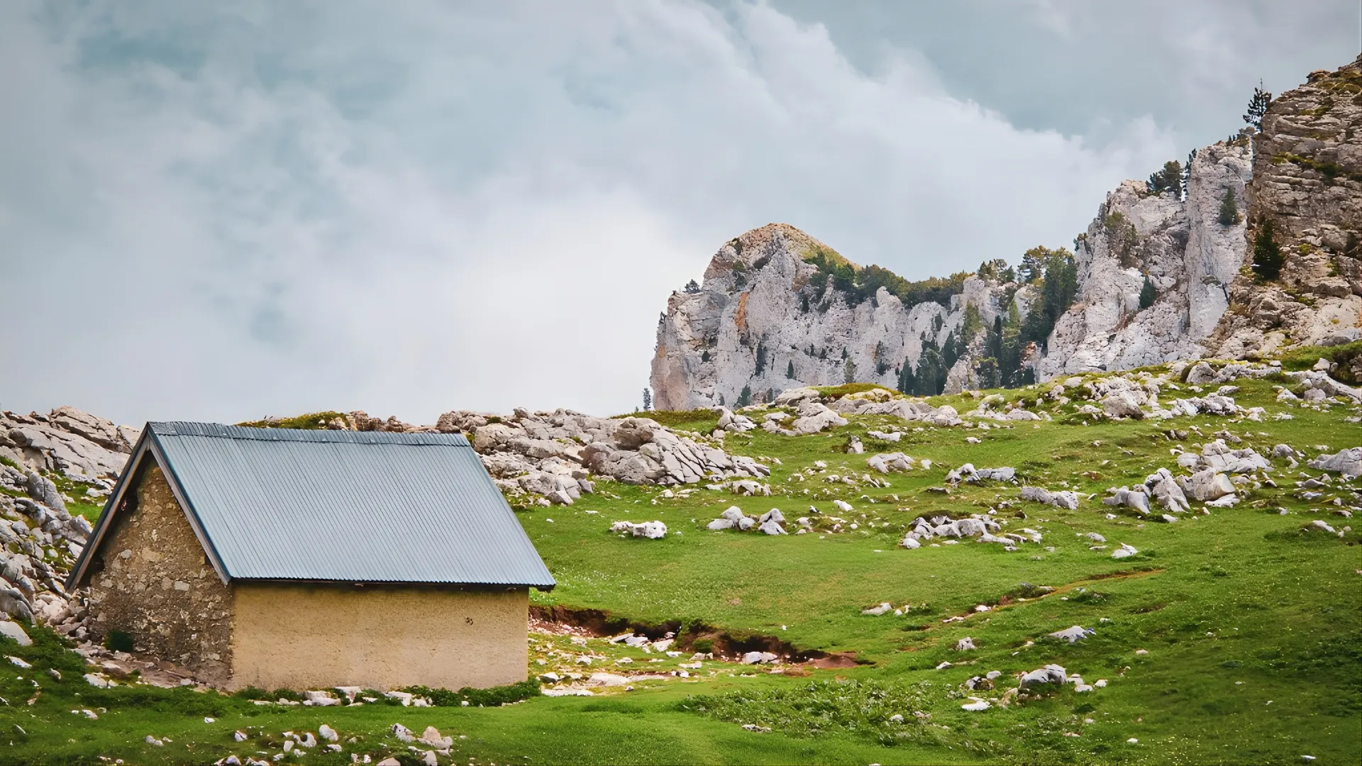 A charming cabin in the heart of nature, surrounded by rocks and lush green meadows.