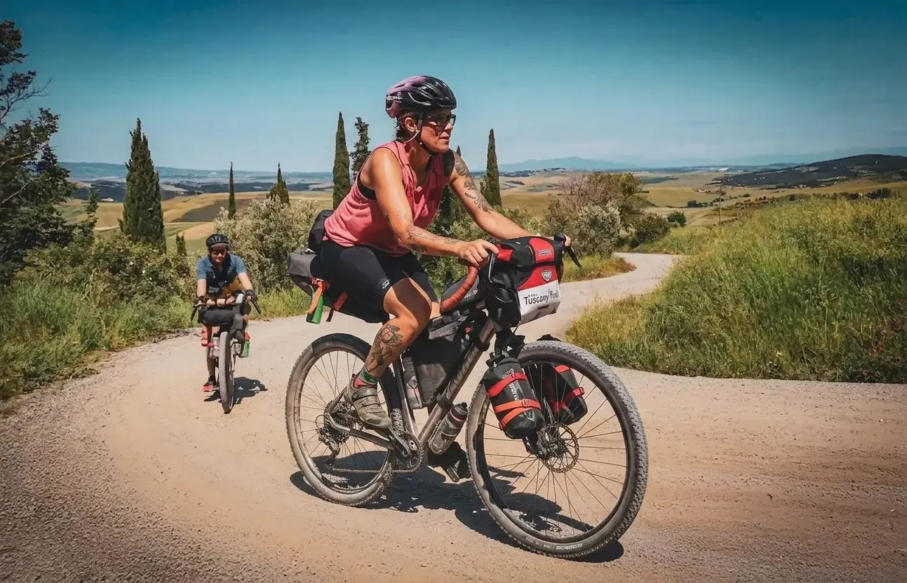 Un couple de cyclistes évolue sur un chemin de gravier sinueux, entouré d'une nature verdoyante et de collines ondulantes.