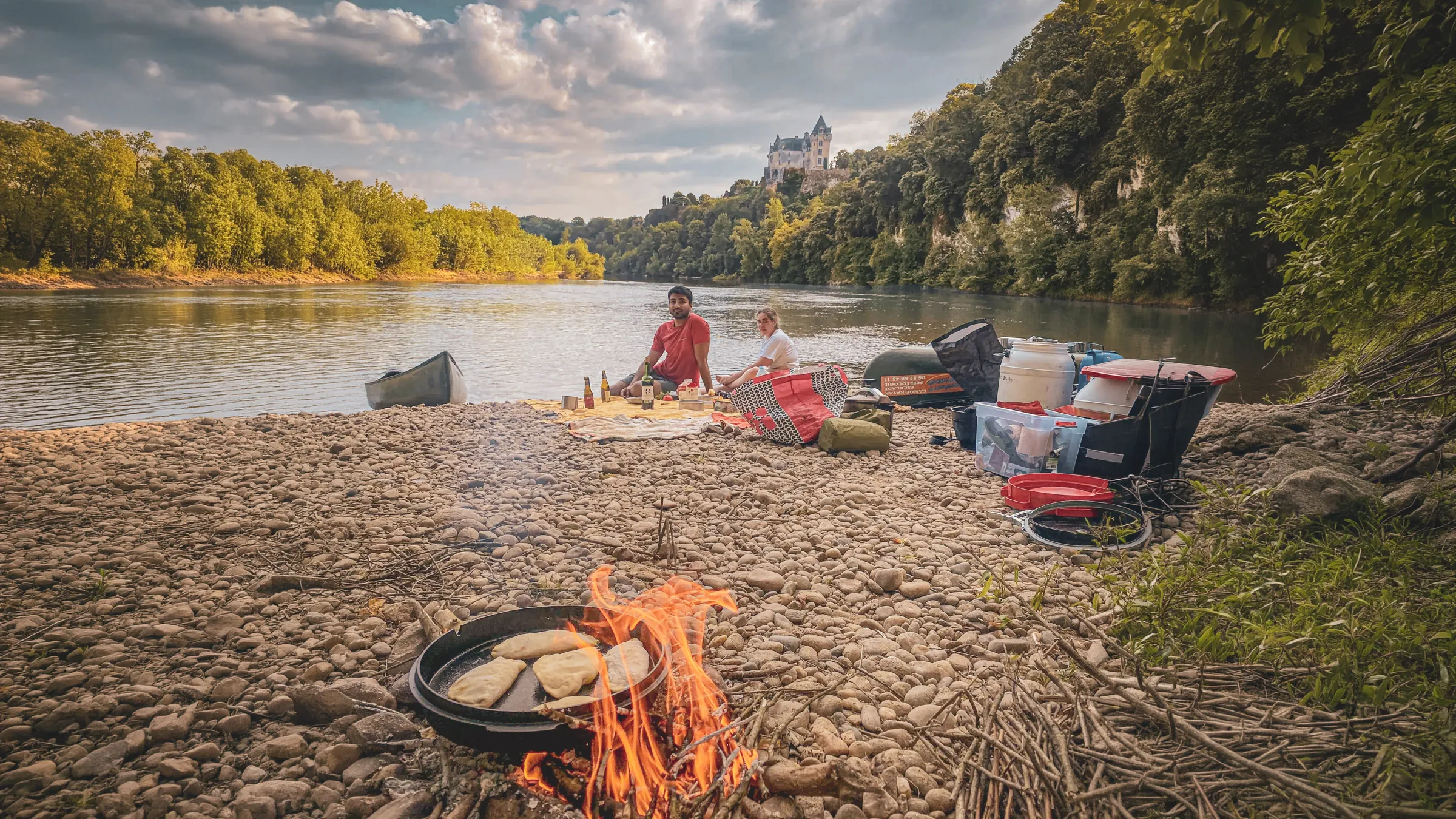 Bivouac au bord de la Dordogne avec feu de camp et canoë, sous un château