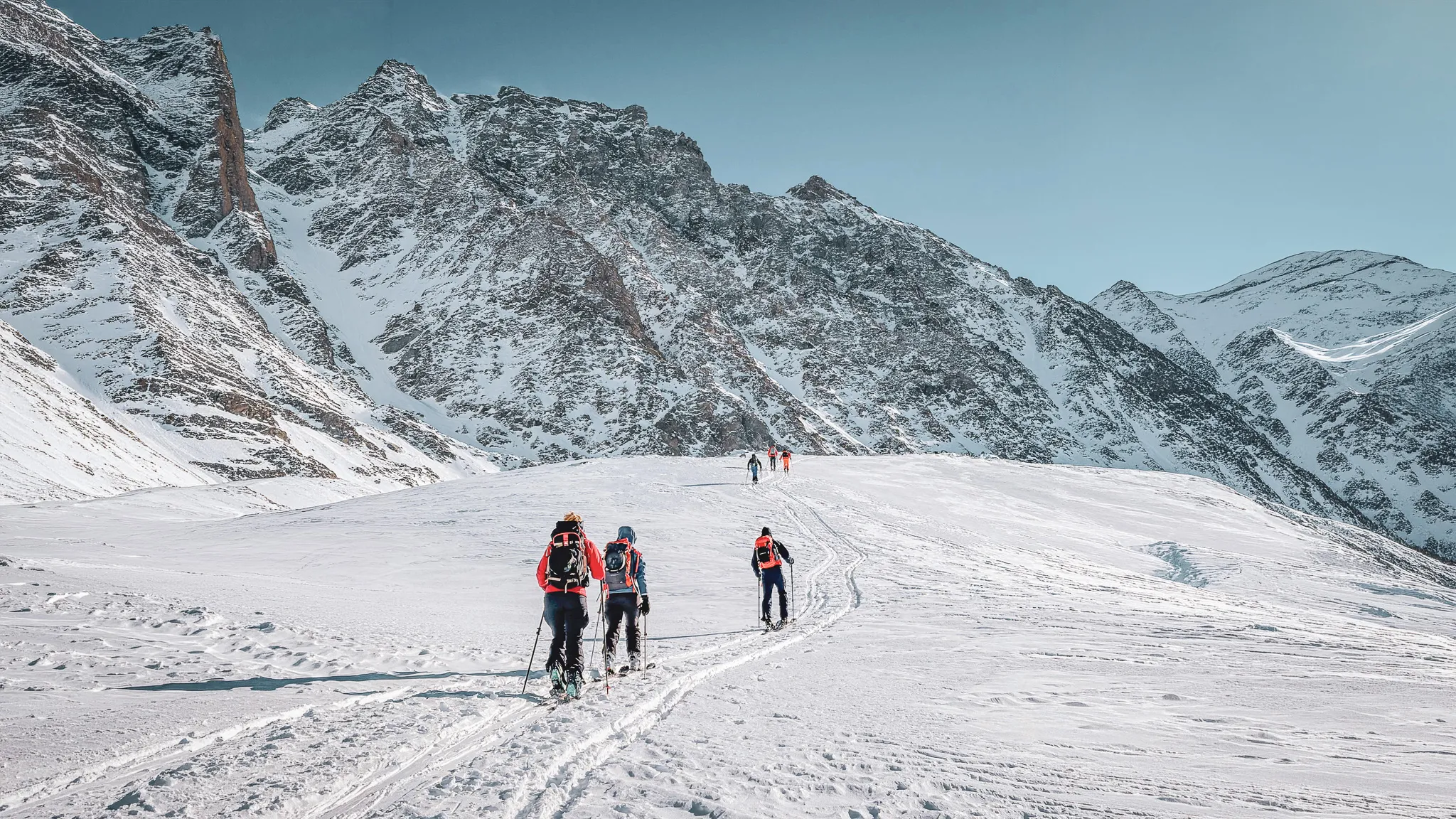 Groep toerskiërs op een uitgestrekt sneeuwveld, omringd door bergen.