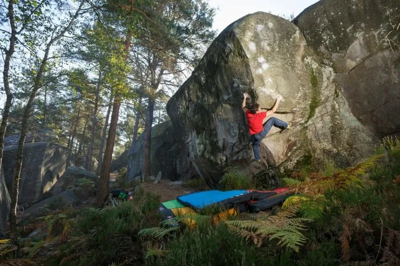 Image dans la forêt d'un homme en train de faire de l'escalade de bloc avec des tapis de sol