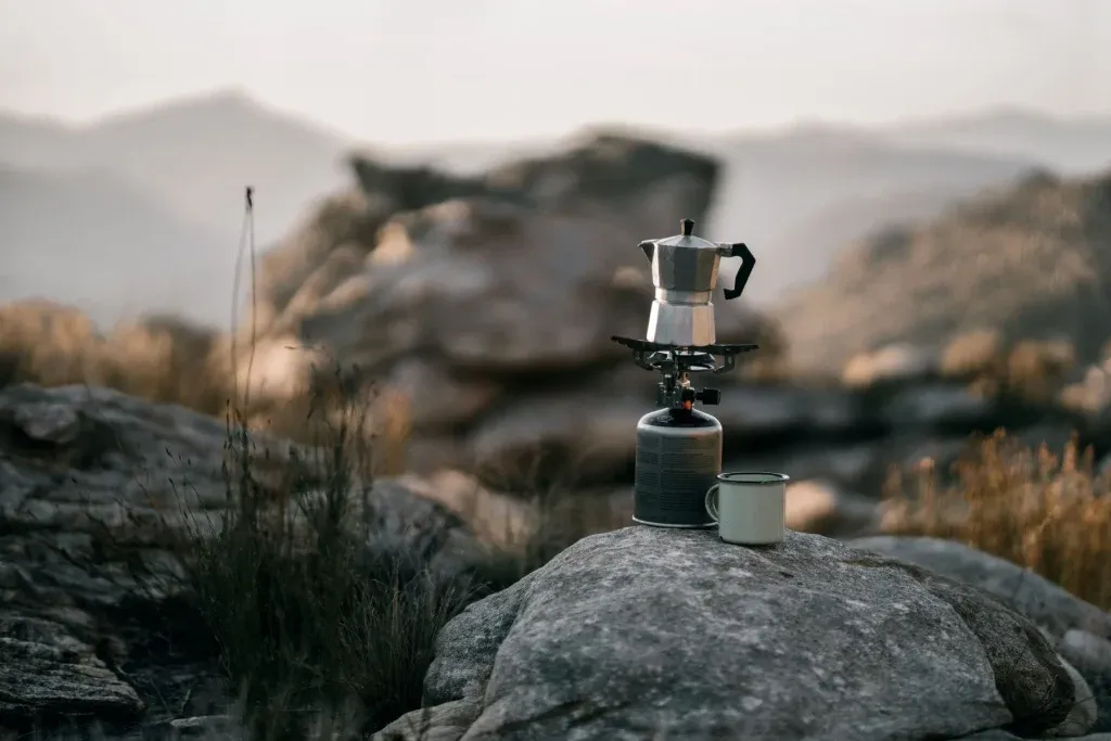 image d'une théière sur un réchaud de bivouac et une tasse posée sur un rocher pour la cuisine en pleine nature