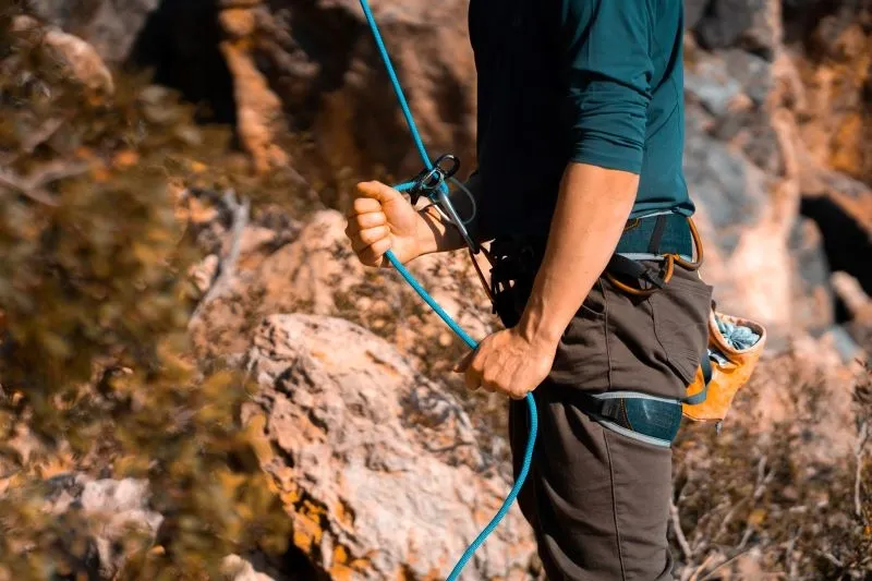 homme avec une corde et un mousqueton devant un rocher