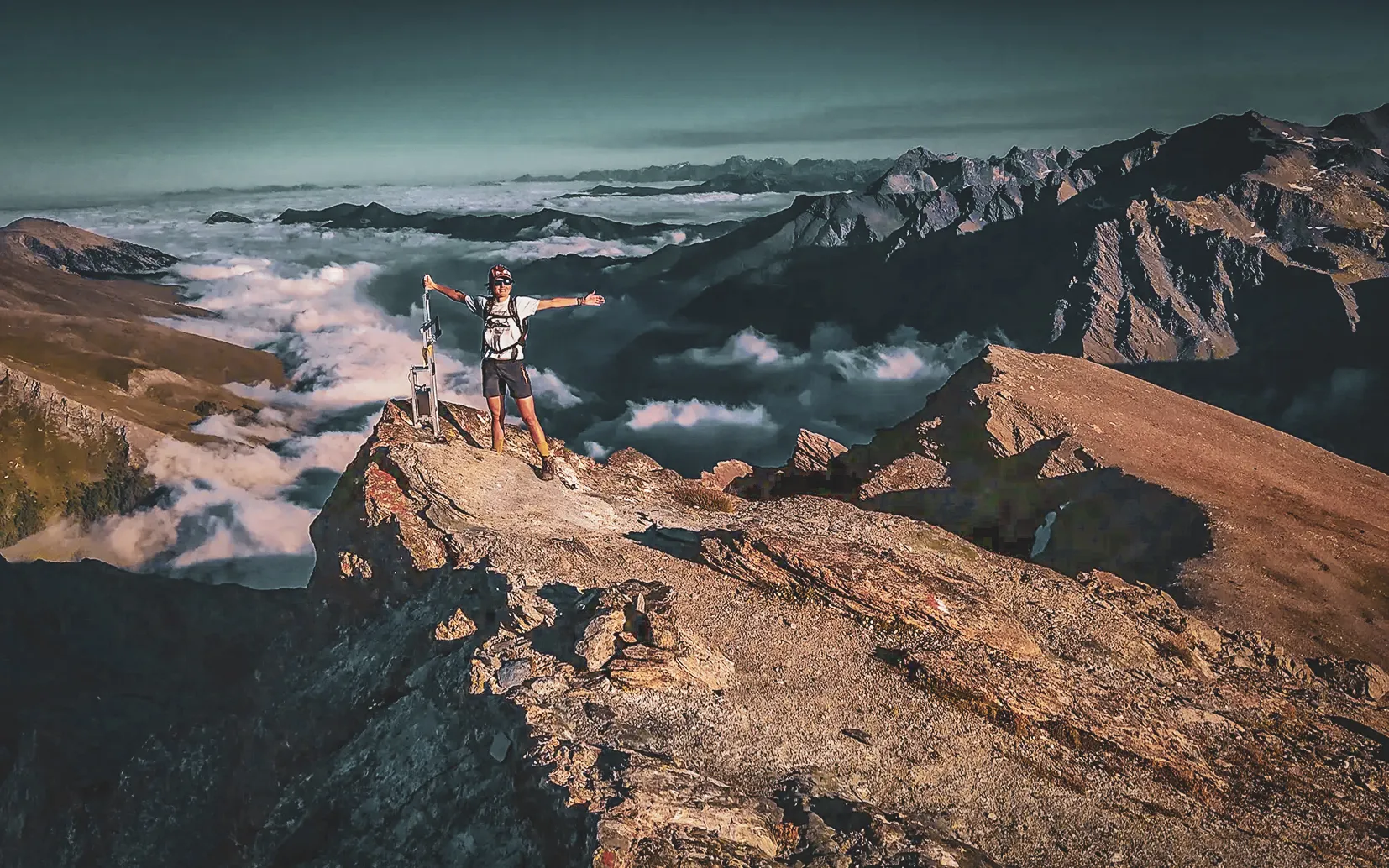 Hiker at the summit of the Pic de Caramantran (3025 m), above the clouds, with views over the French and Italian Alps.