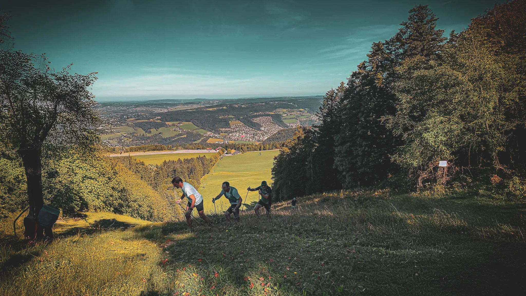 A group of adventurers climb a green hill with a panoramic view over the valley.