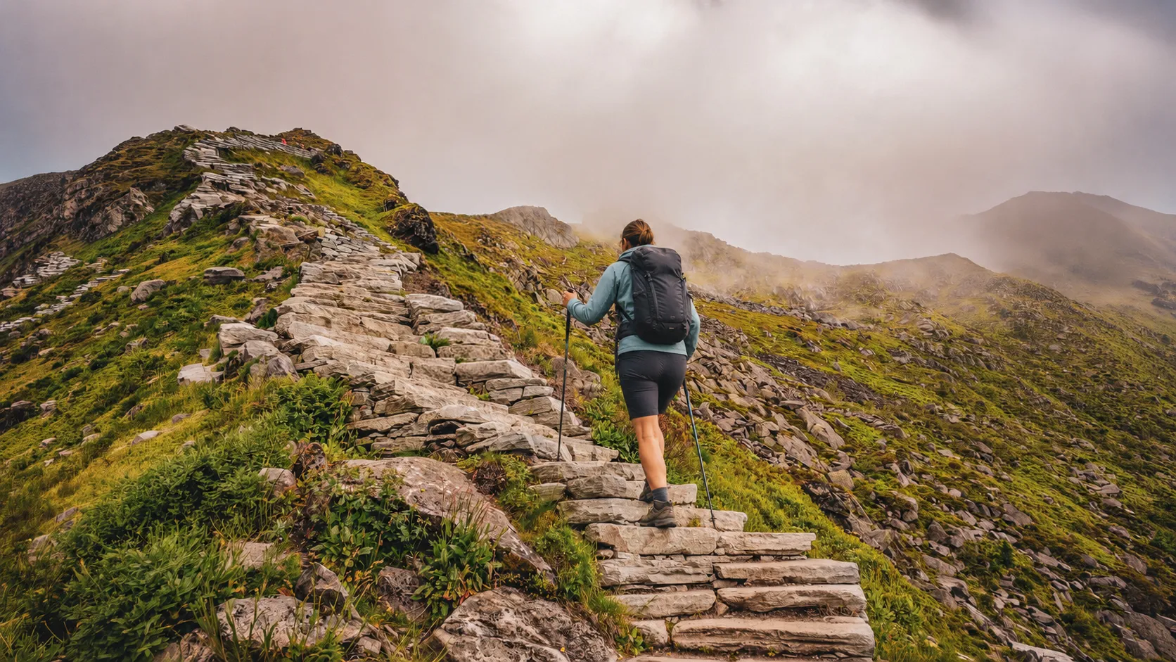 A hiker climbs stone steps surrounded by lush green landscapes on the Lofoten Islands.