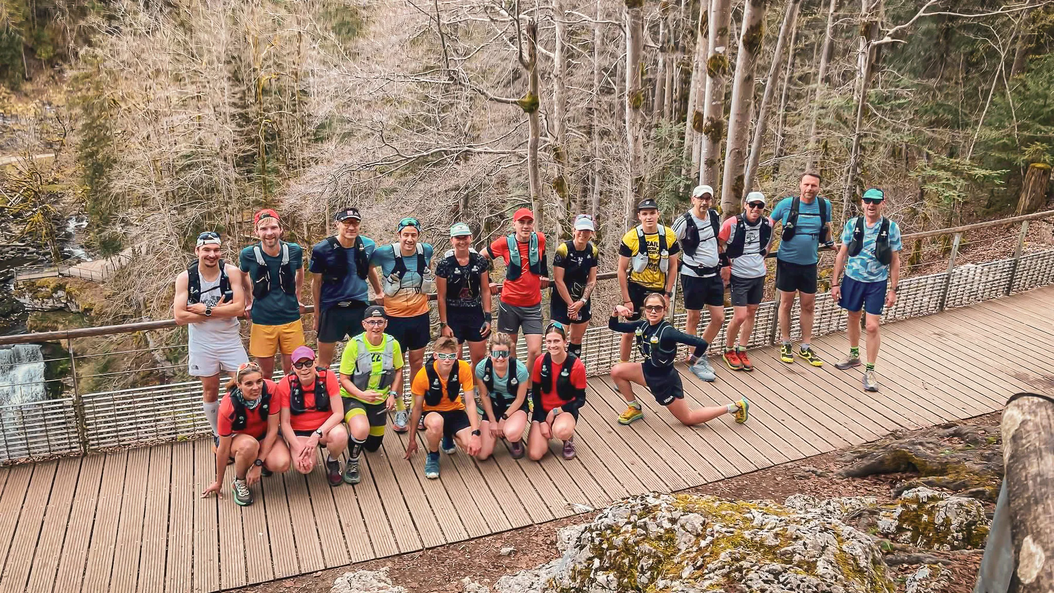 An enthusiastic group of runners on a wooden trail surrounded by lush green countryside in the Jura.