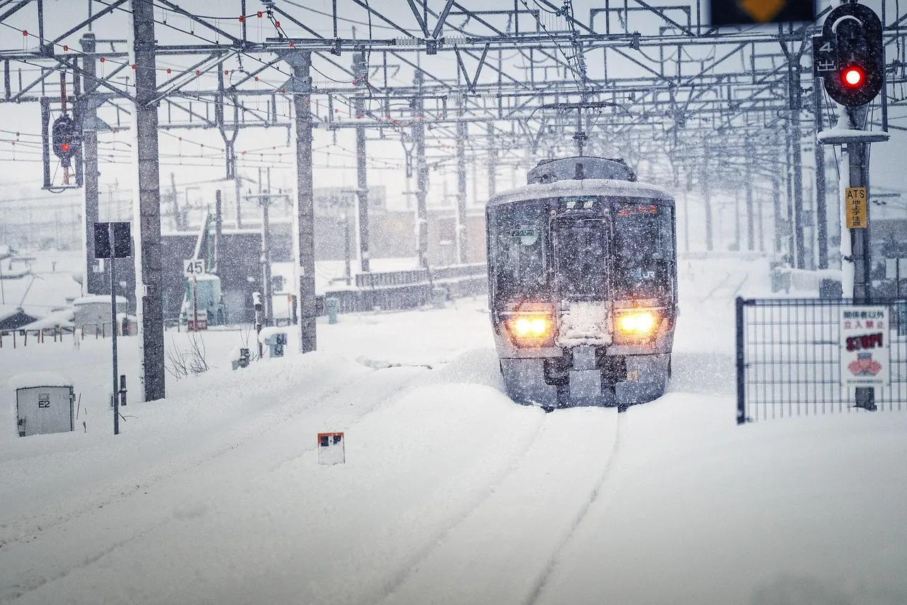 Un train arrive en gare sous une forte chute de neige, phares allumés