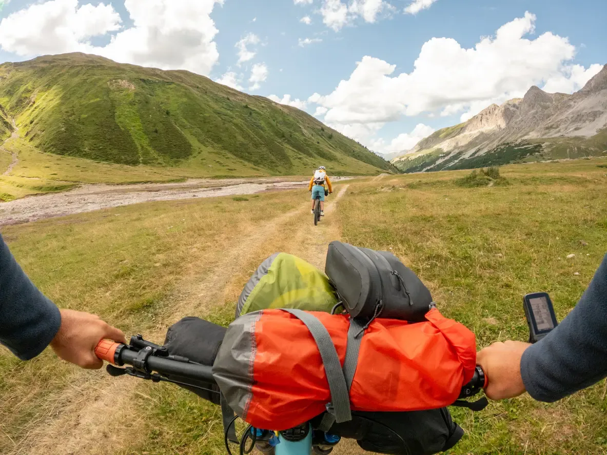 Deux cyclistes chargés de sacoches roulent sur un sentier au fond d'une vallée de montagne